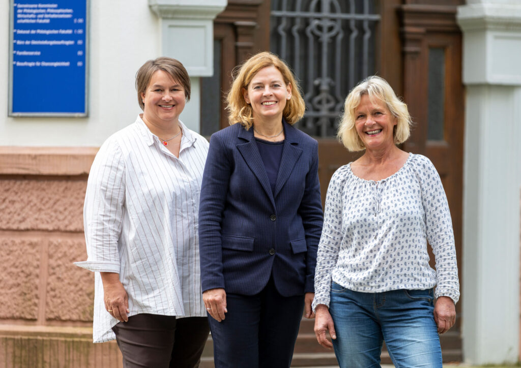 Drei Frauen stehen lächelnd vor einem alten Gebäude