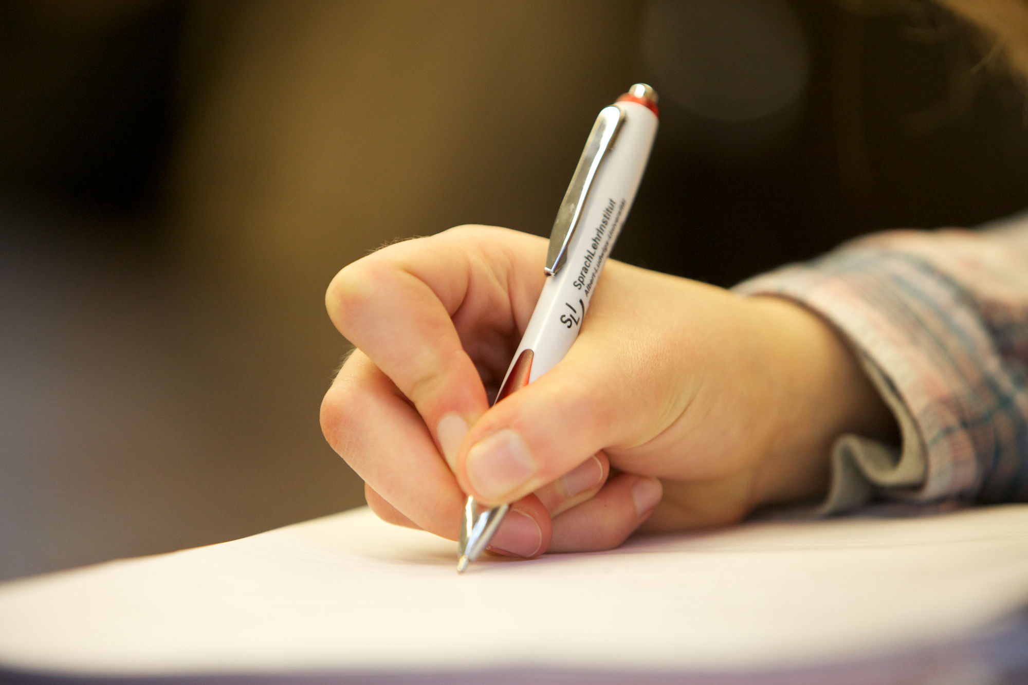 One hand holds a pen from the language teaching institute at the University of Freiburg and writes on a sheet of paper.