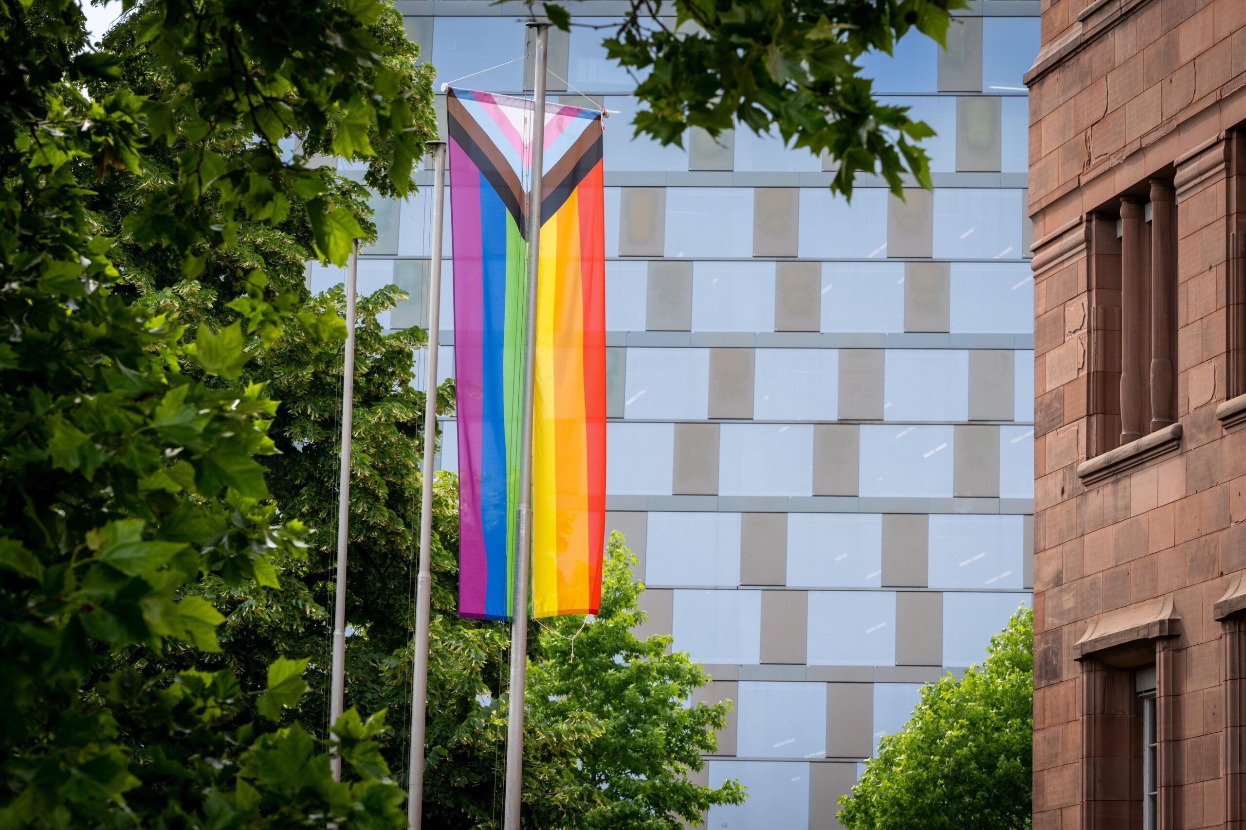 The Pride flag hangs on the flagpole in front of KG 1, with the University Library in the background.