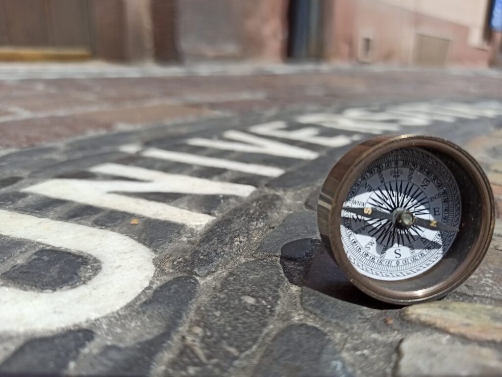 A compass is lying on the ground, next to a white lettering saying "Universitas"