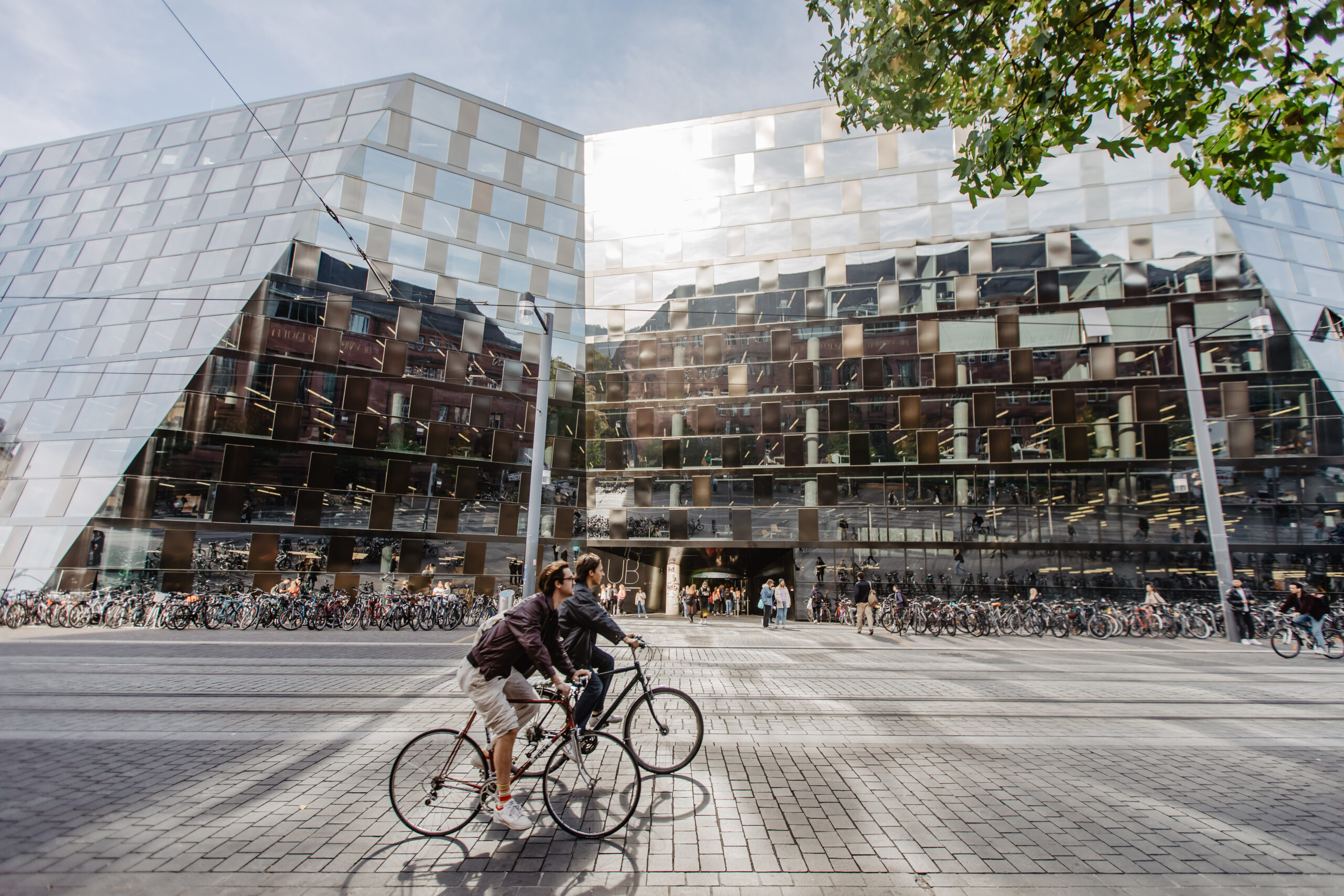 Two people ride past the university library on their bicycles.