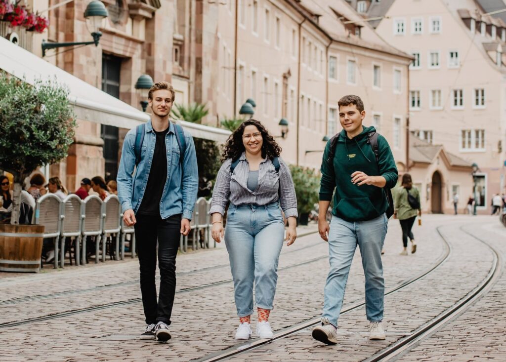 Drei junge Menschen gehen die Bertoldstraße entlang. Im Hintergrund der Turm des Freiburger Münsters.