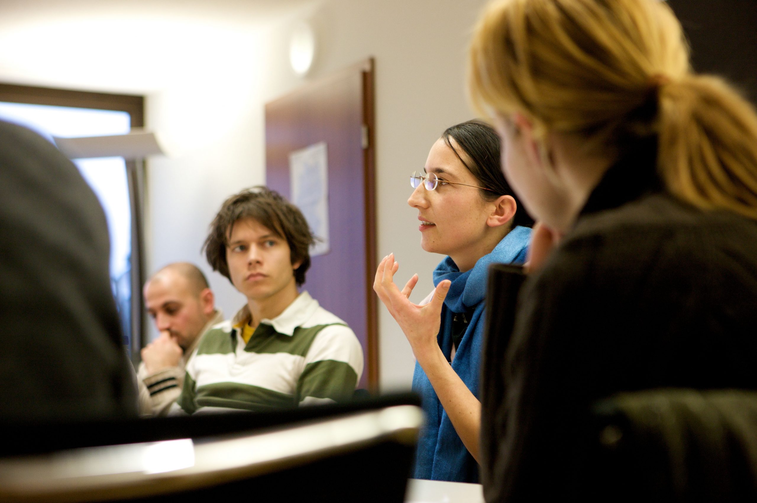 The picture shows a group of people sitting and discussing in a workshop or seminar room.