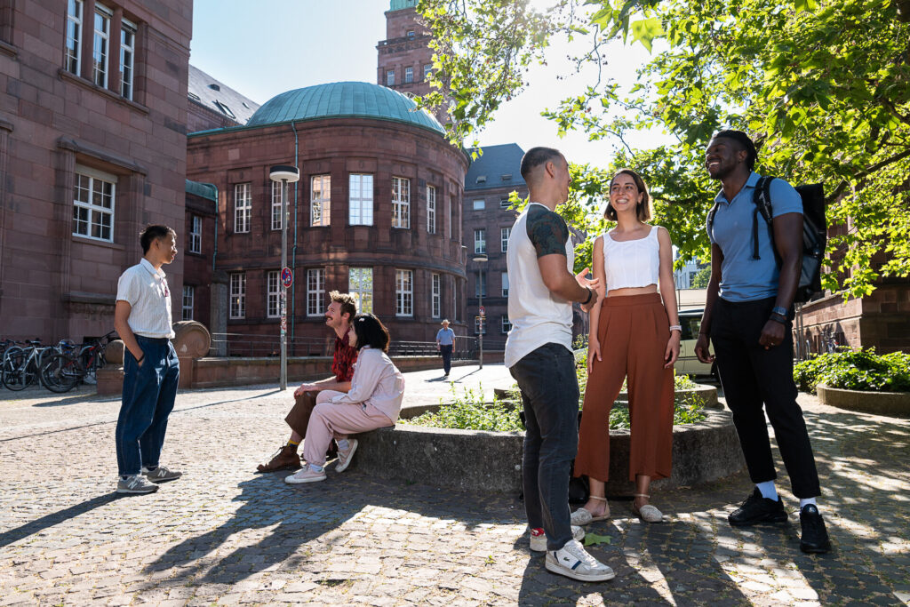 Weibliche und männliche Studierende verschiedener Herkünfte vor dem Kollegiengebäude I.