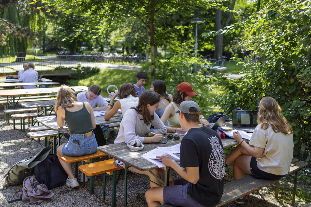 Studierende arbeiten im Freien gemeinsam an Tischen sitzend