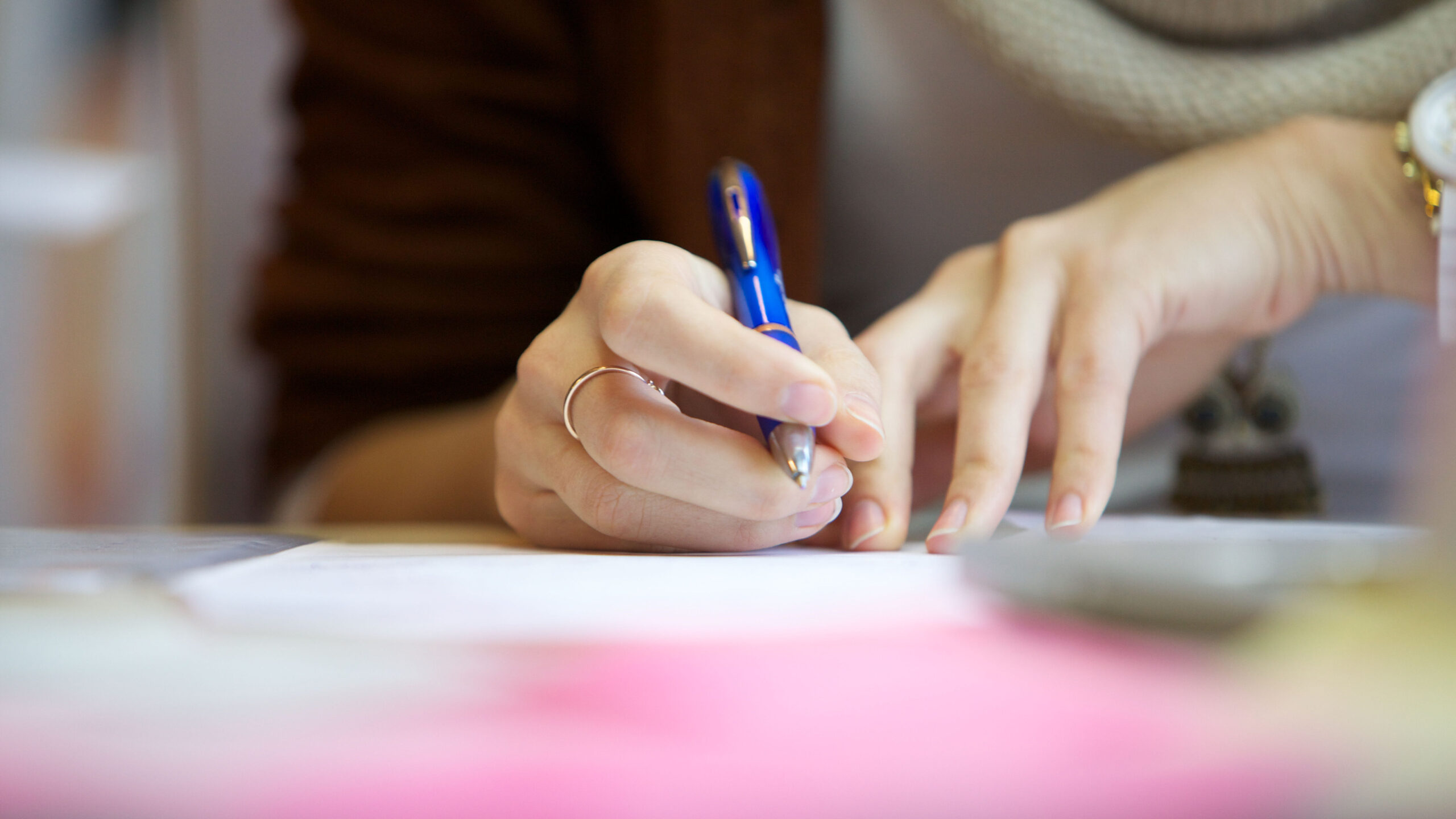 A woman holds a blue pen in her hand and is about to write something down.