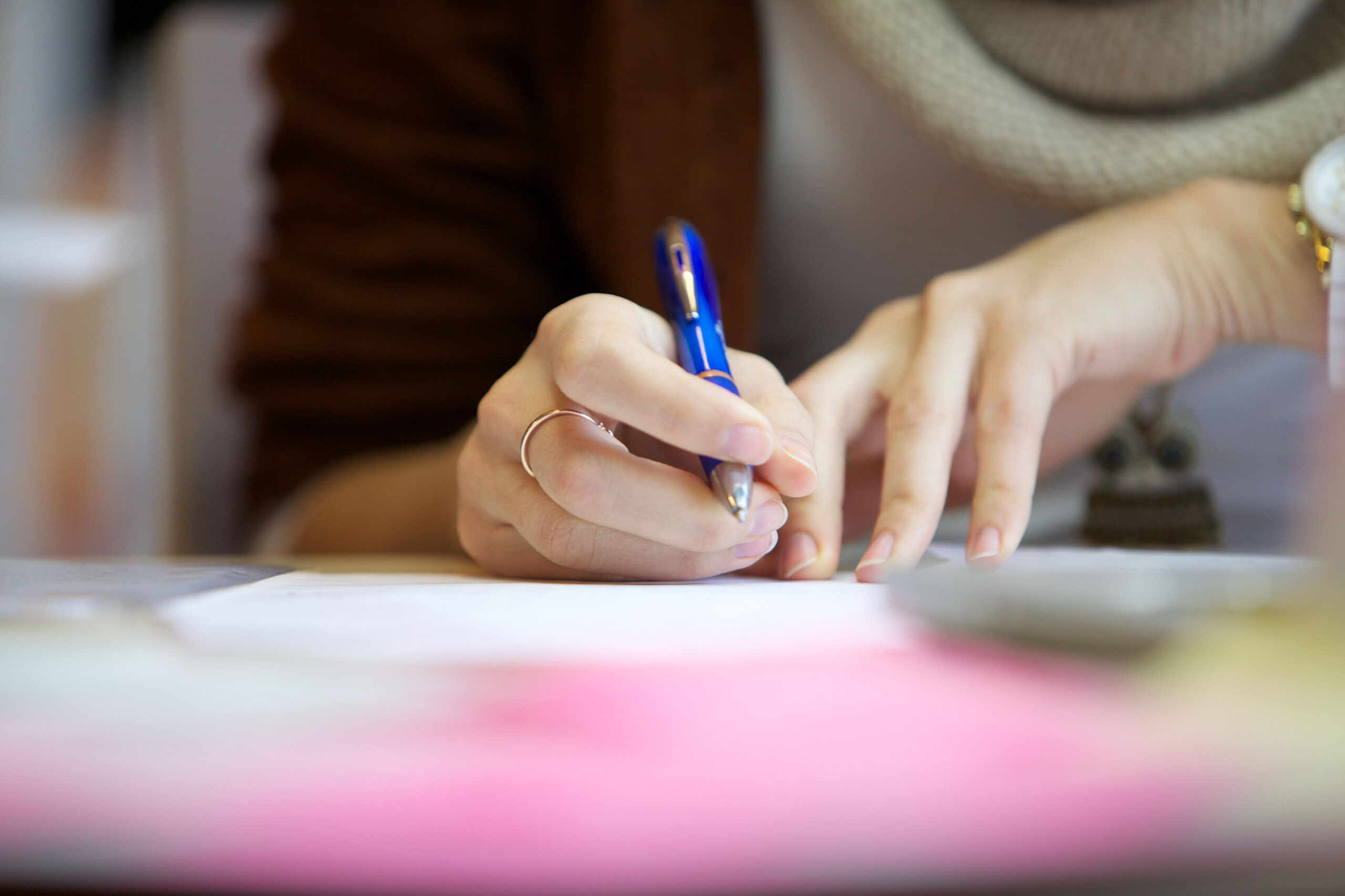 The picture shows a hand, writing something with a blue pencil.   