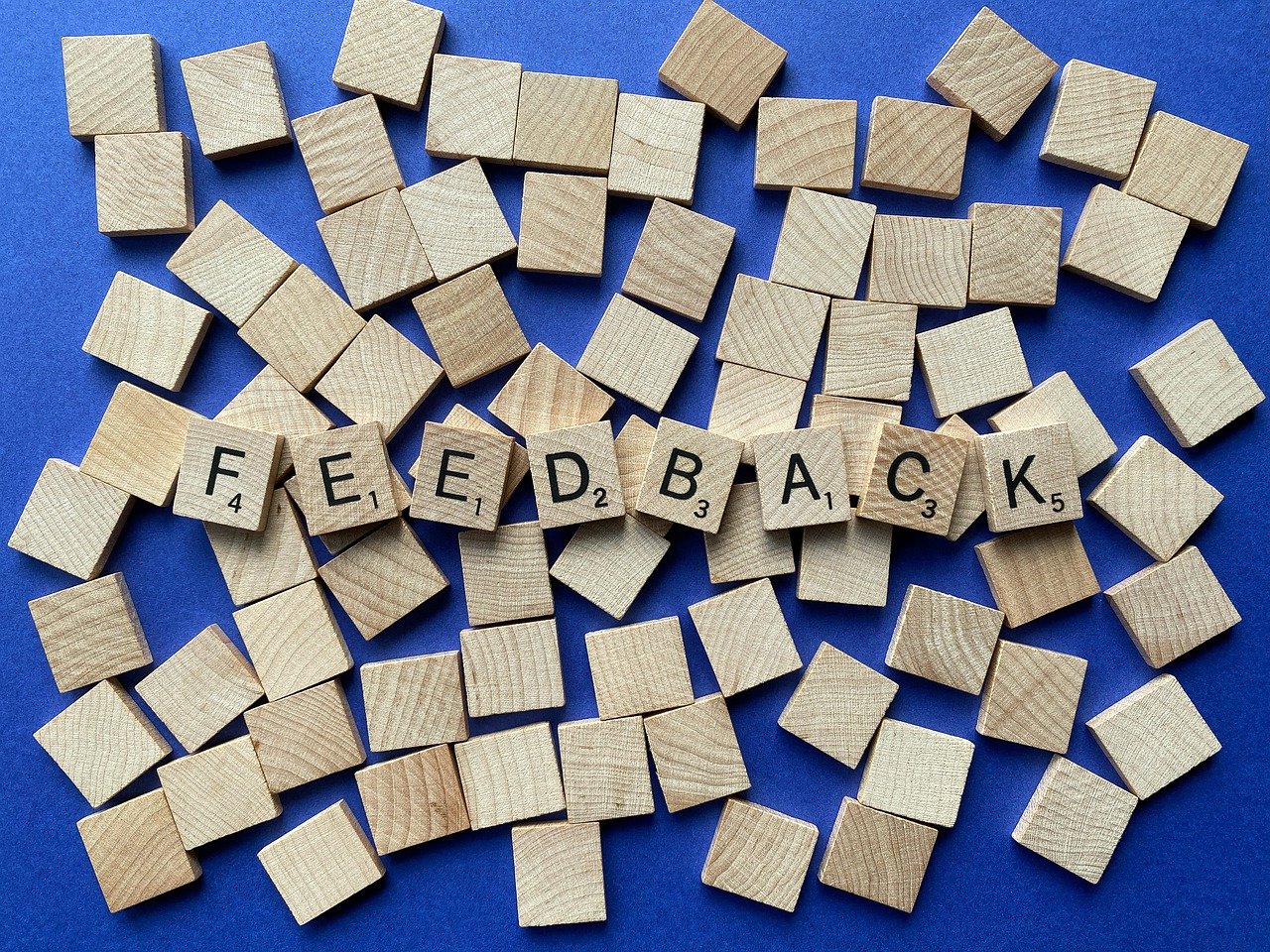 Wooden blocks distributed on a blue background. Some blocks are labelled with letters and numerical values and form the word: feedback.