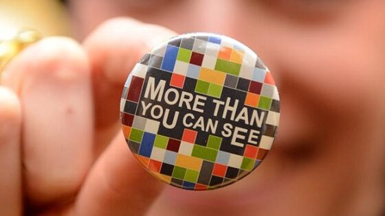 A woman holds a button for the camera. The button says: More than you can see.