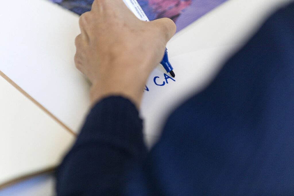 Hand, Stift, Papier und eine schreibende Person