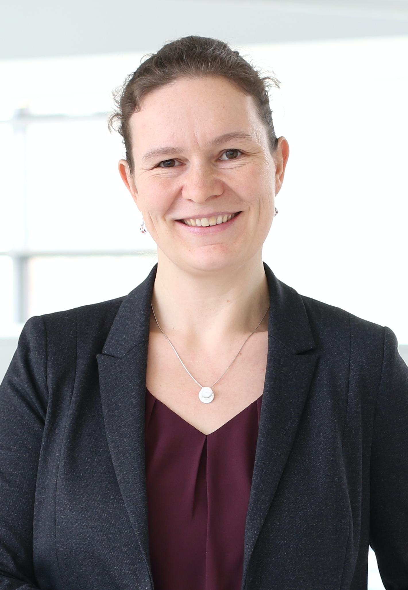 portrait of Dr. Mareike Albert. She is a white-colored woman, her hair is tied back. She wears a dark blazer, a red blouse and a silver necklace. She smiles friendly.