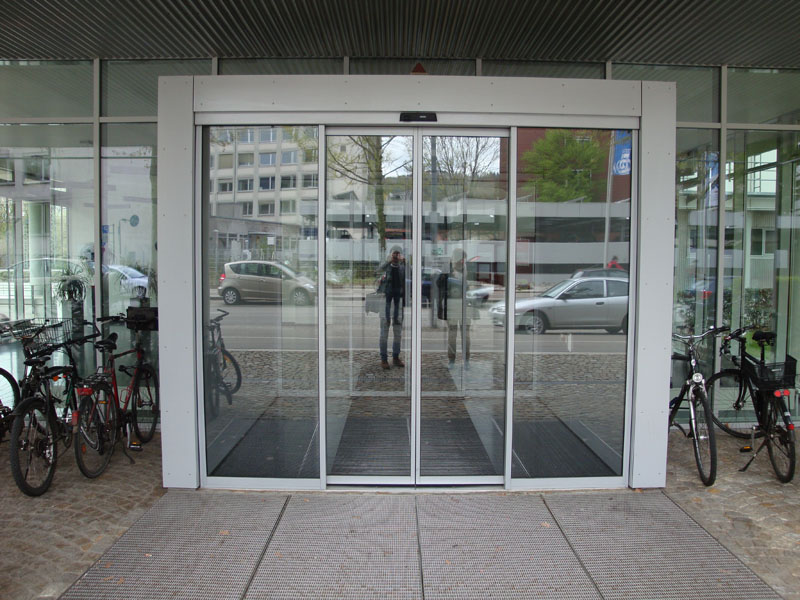 Eine große, automatische Glastür ist umgeben von abgestellten Fahrrädern
