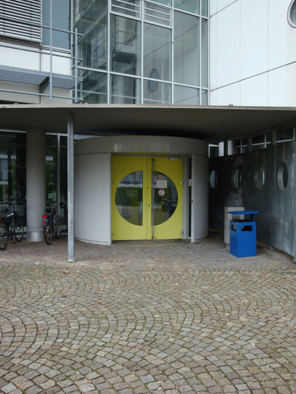 Eine aus zwei Flügeln bestehende gelbe Tür wird von einem größeren Flachdach geschützt.