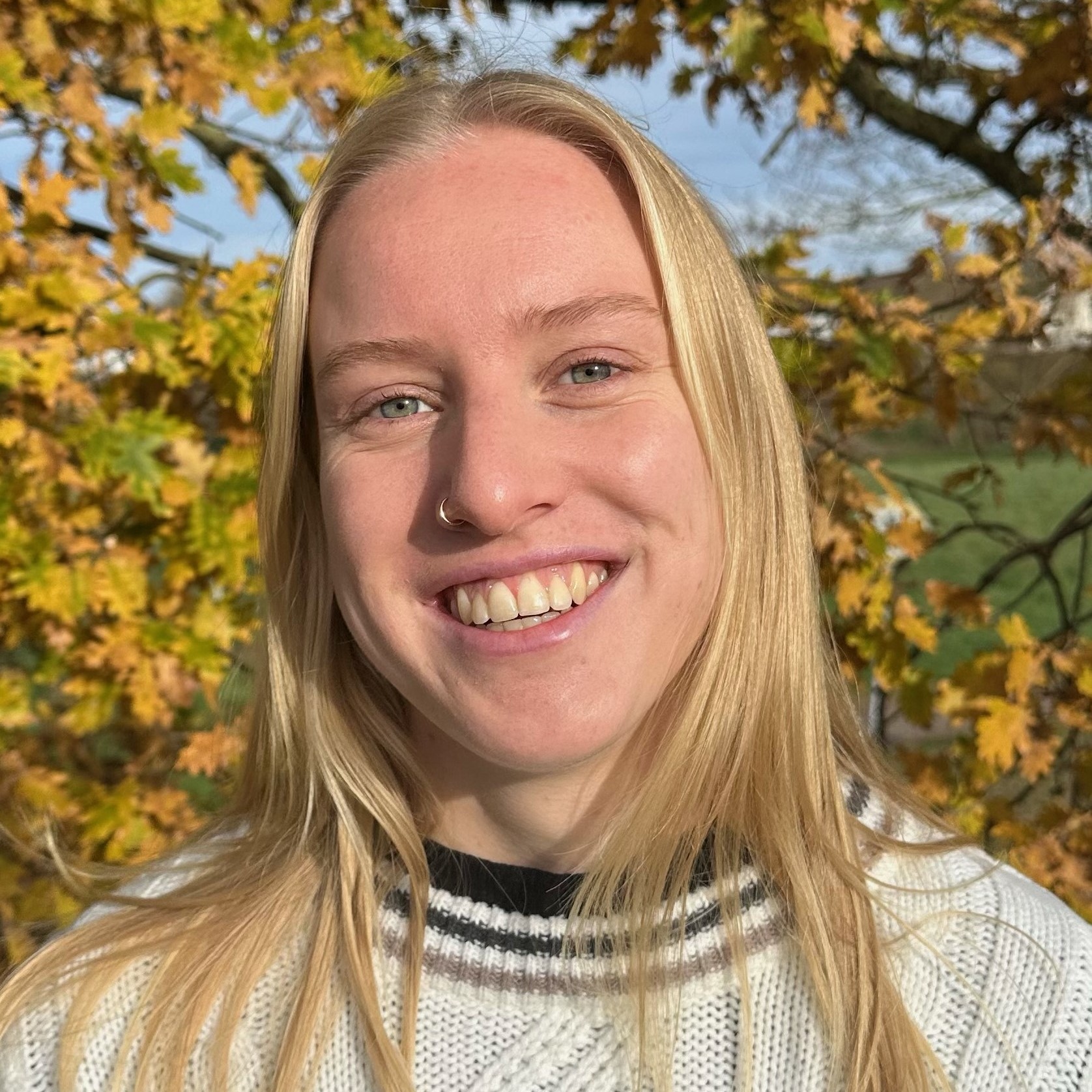 Portrait von Alicia Kling. Im Hintergrund ist ein Baum mit einigen gelb-braunen und einigen grünen Blättern