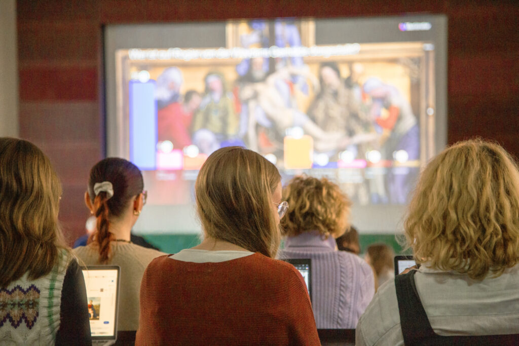 Studenten arbeiten am Laptop vor einem großen Bildschirm.