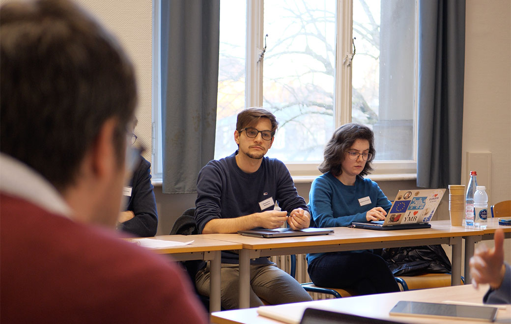 Drei junge Menschen sitzen an Tischen vor Laptops