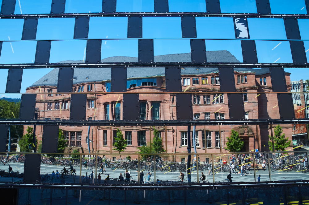 Die Fassade des Kollegiengebäude 1 spiegelt sich in der Glasfassade der Universitätsbibliothek