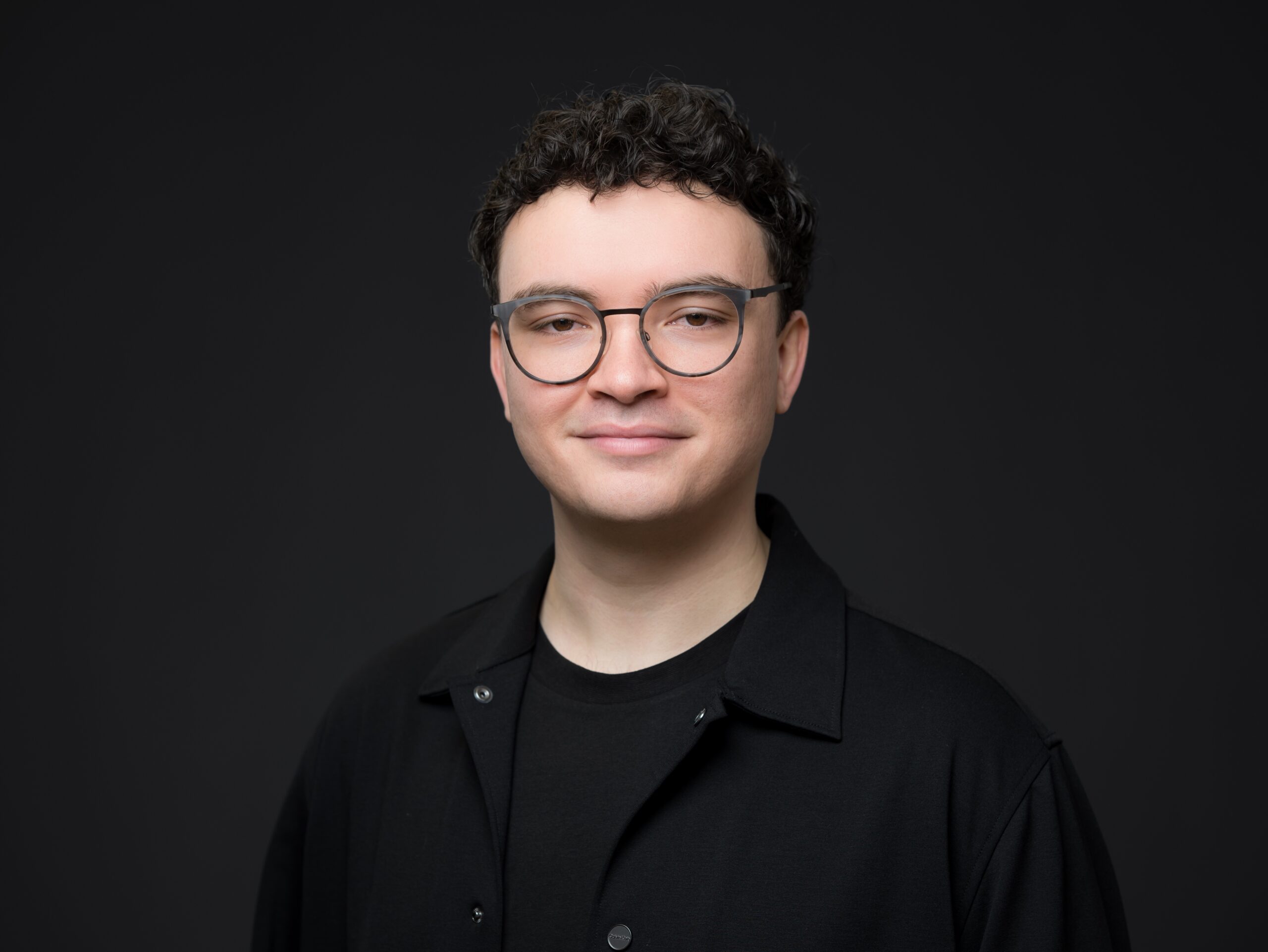 Ein junger Mann mit Brille und kurzem, dunklem und lockigem Haar.