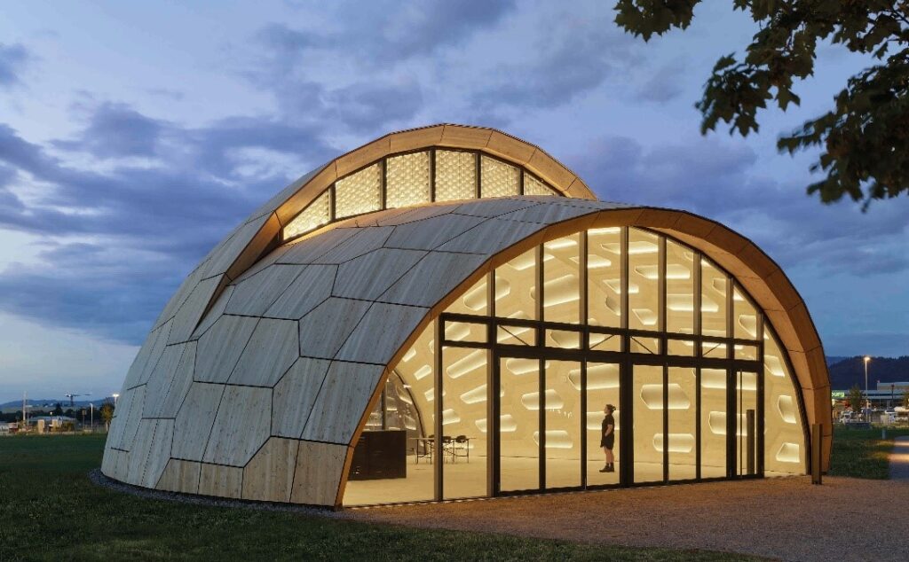 Ein erleuchtetes Gebäude, geformt wie eine Muschel, mit einer wabenförmigen Außenhaut