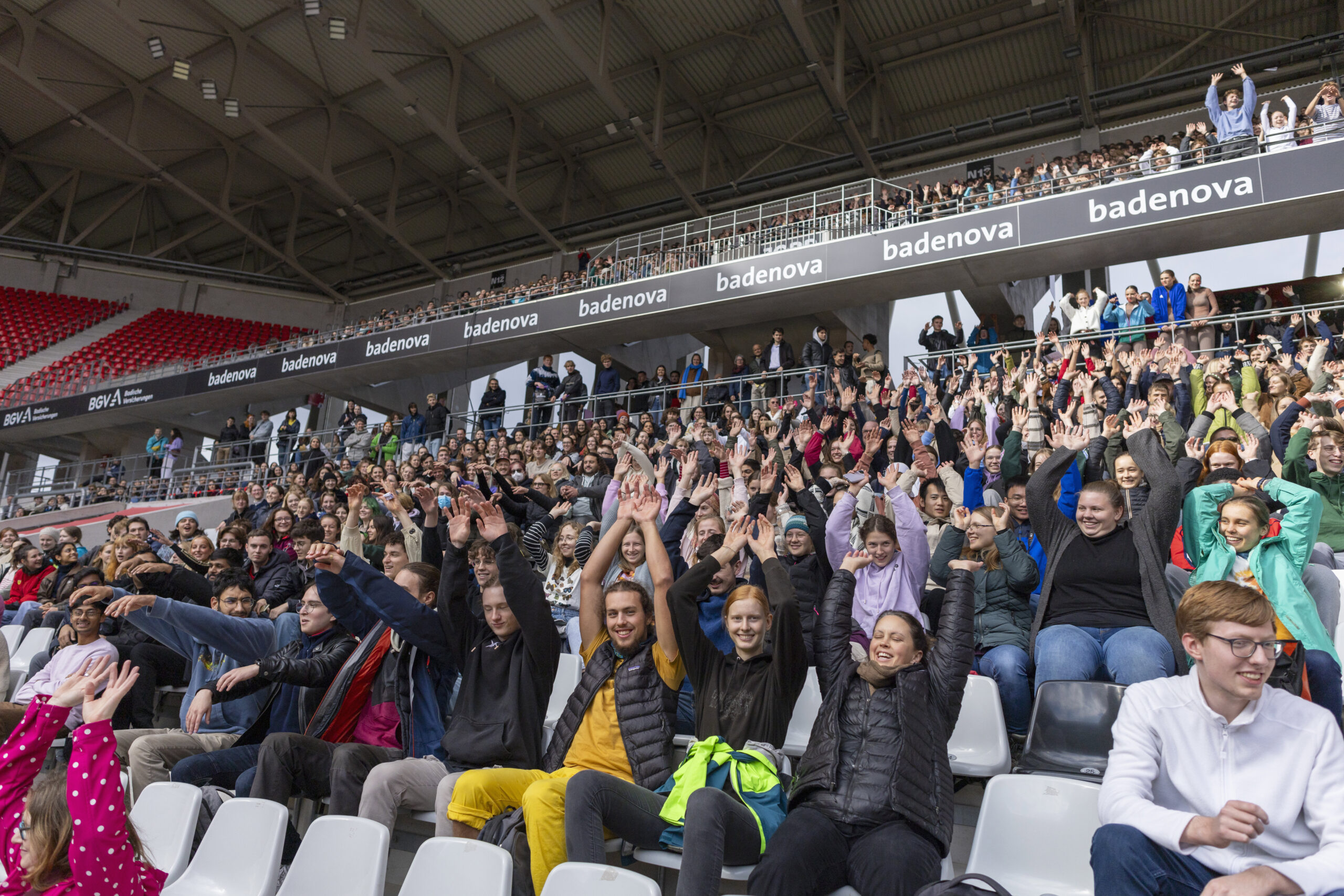 Studierende heben auf der Tribüne des Europa-park Stadions die Hände.