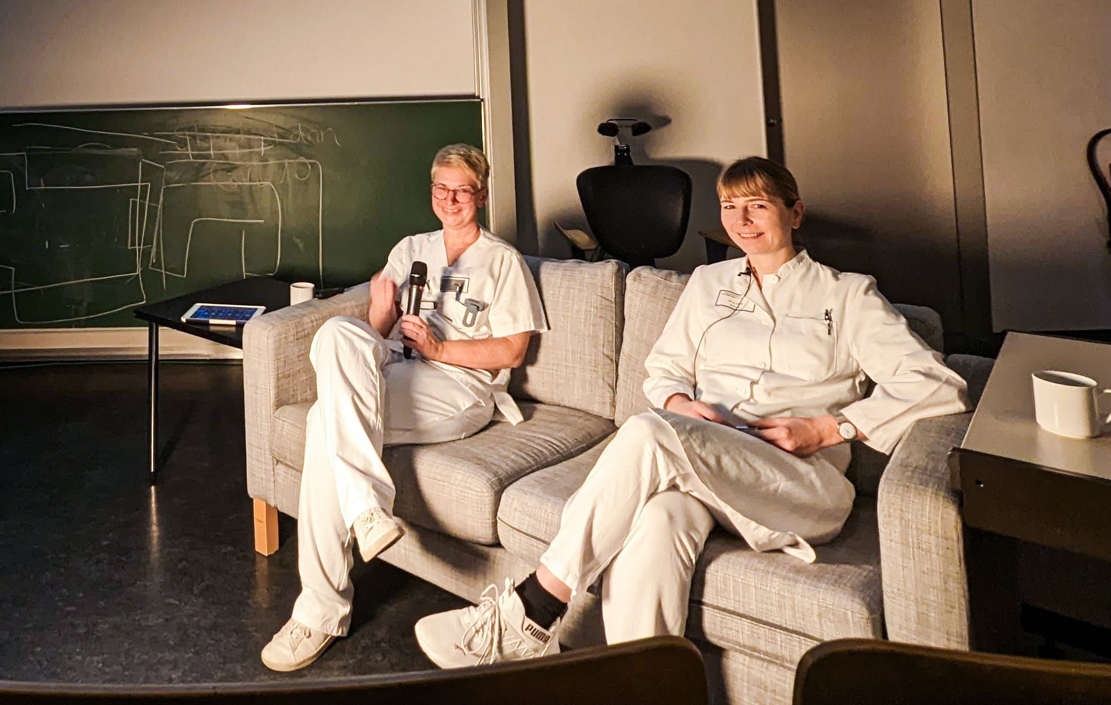 Zwei Frauen sitzen auf einem Sofa in einem Podcast-Setting.