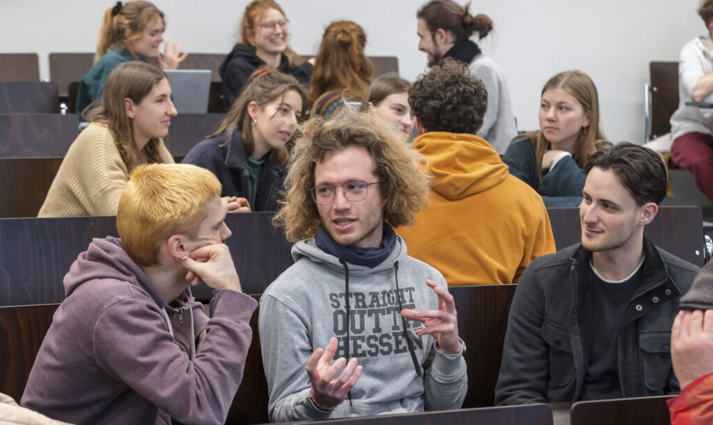 Mehrere Studierende diskutieren in einem Hörsaal.