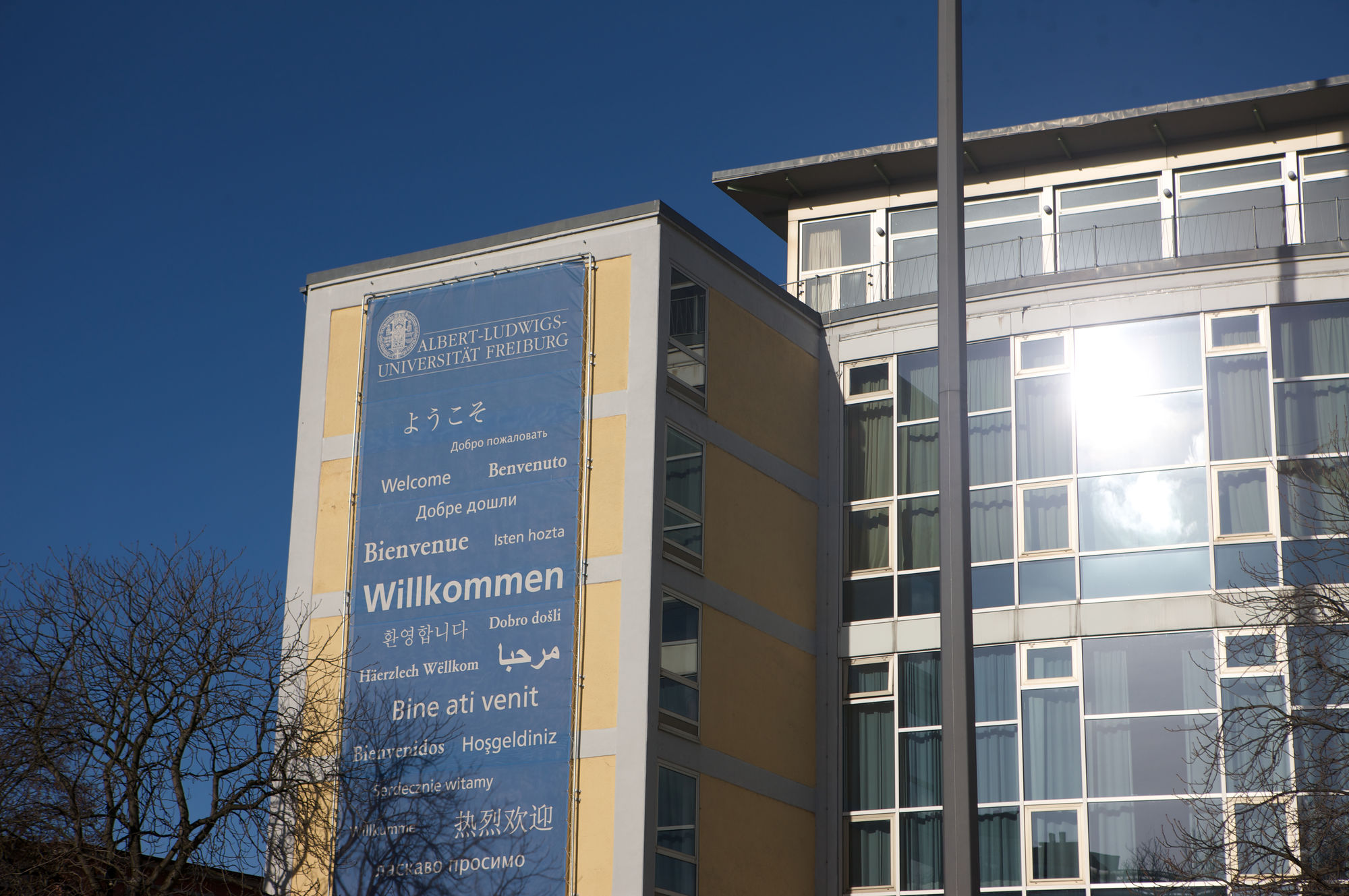 Das Rektoratsgebäude der Universität Freiburg mit einem Banner auf dem "Willkommen" in verschiedene Sprachen steht.