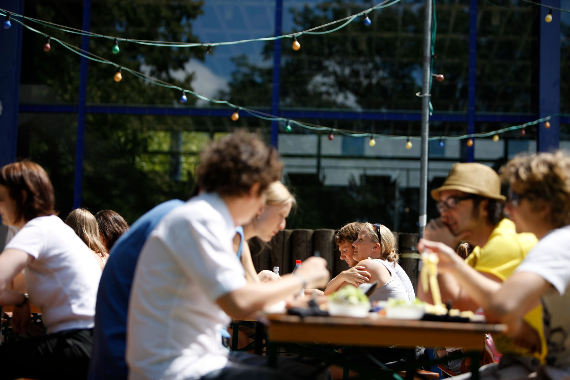 Studierende sitzen im Sonnenschein im Außerbereich der Mensa Rempartstraße beim Mittagessen.